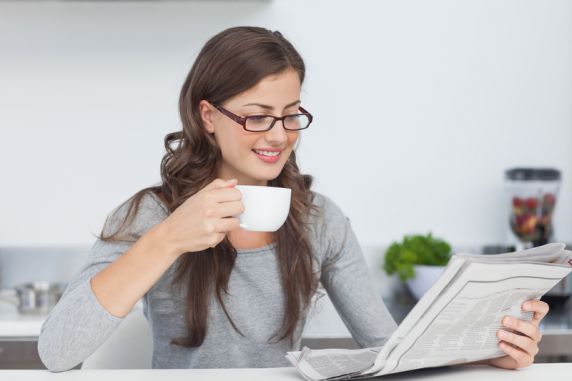 Frau mit Brille liest Zeitung und hält eine Kaffeetasse in der Hand